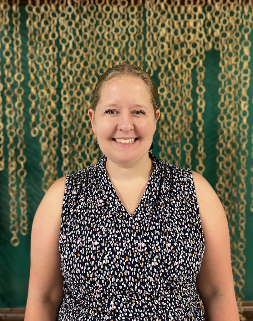 Smiling woman in sleeveless black and white top stands in front of a patterned curtain