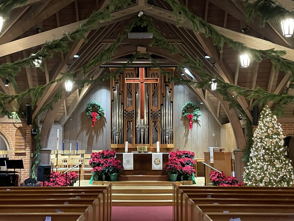 A church sanctuary decorated for Christmas with wreaths, red poinsettias and a tree