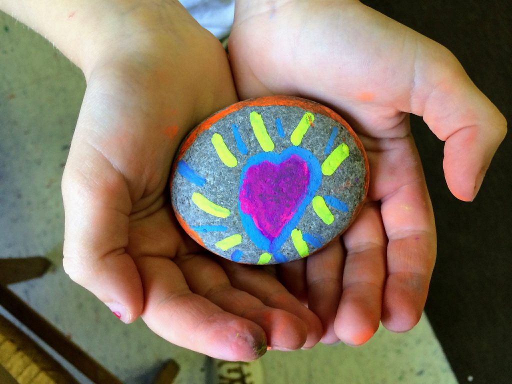 Two hands holding a rock with a heart painted on it