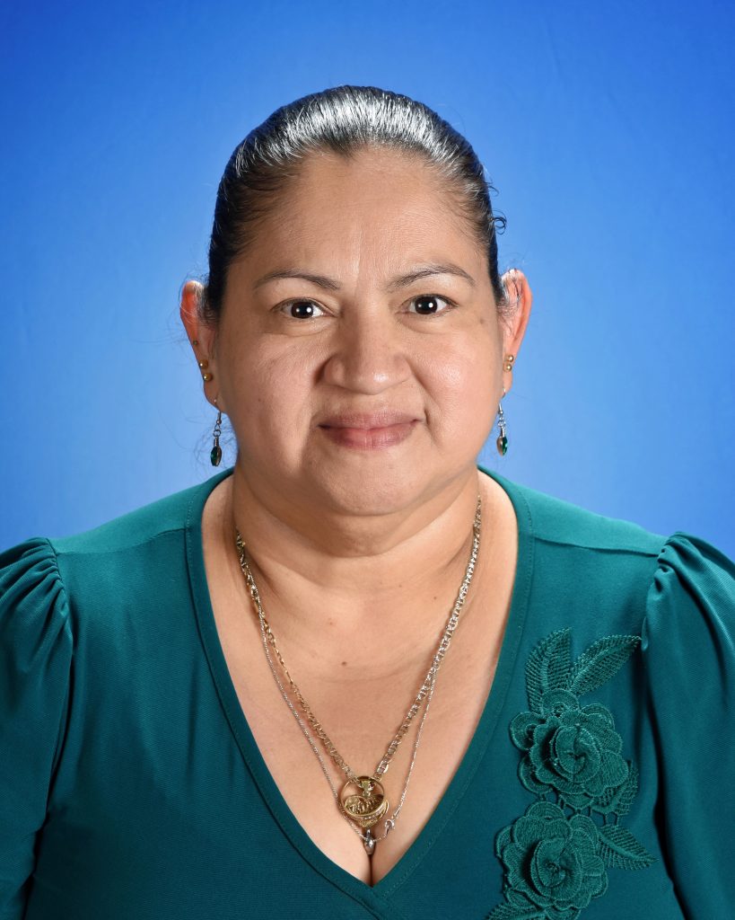 A women with hair pulled back, wearing a teal shirt, in front of a blue background
