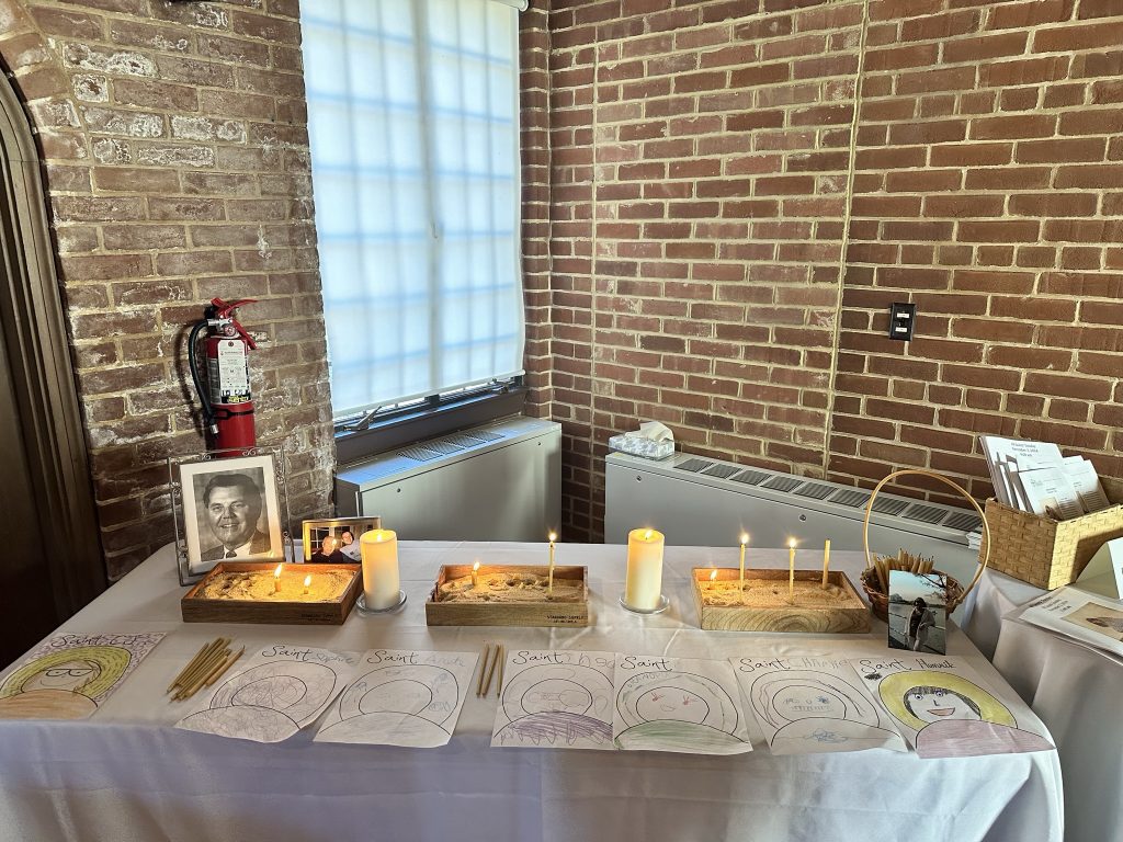 A table with candles and paper worksheets with Saints names