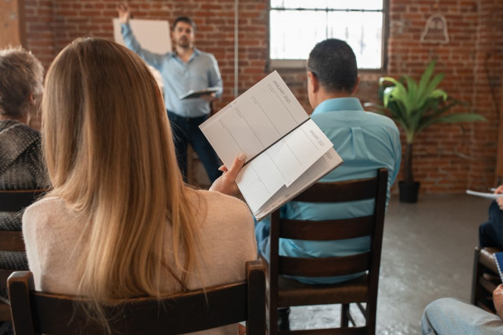 A group of adults sit in chairs. A leader stands in front of the group