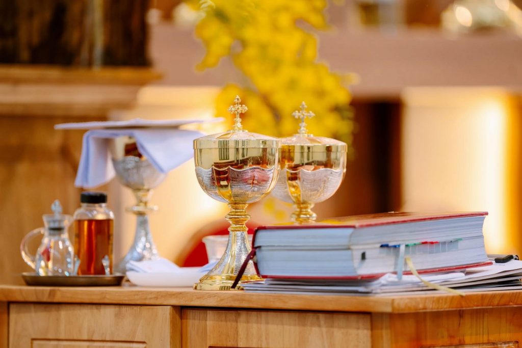 A wooden table is set with a bible and two chalices.