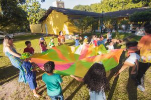 Children standing outdoors in a circle holding a colorful parachute