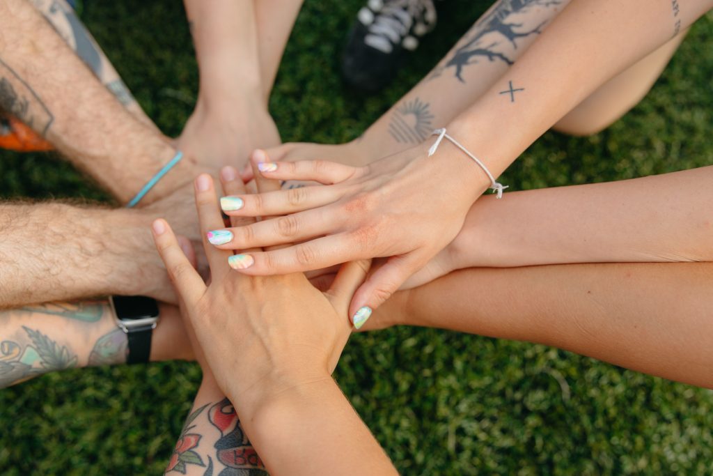 A group of people, some with tattoos, stack hands on top of one another