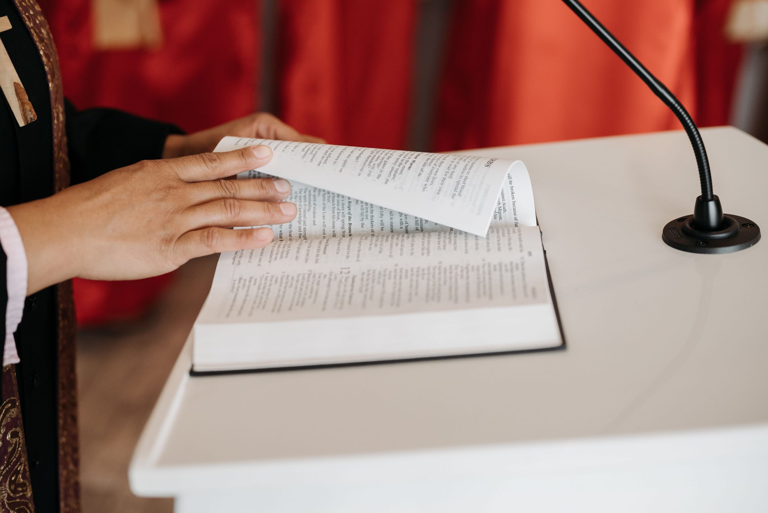 A bible sits on a pulpit. A hand is visible turning the page